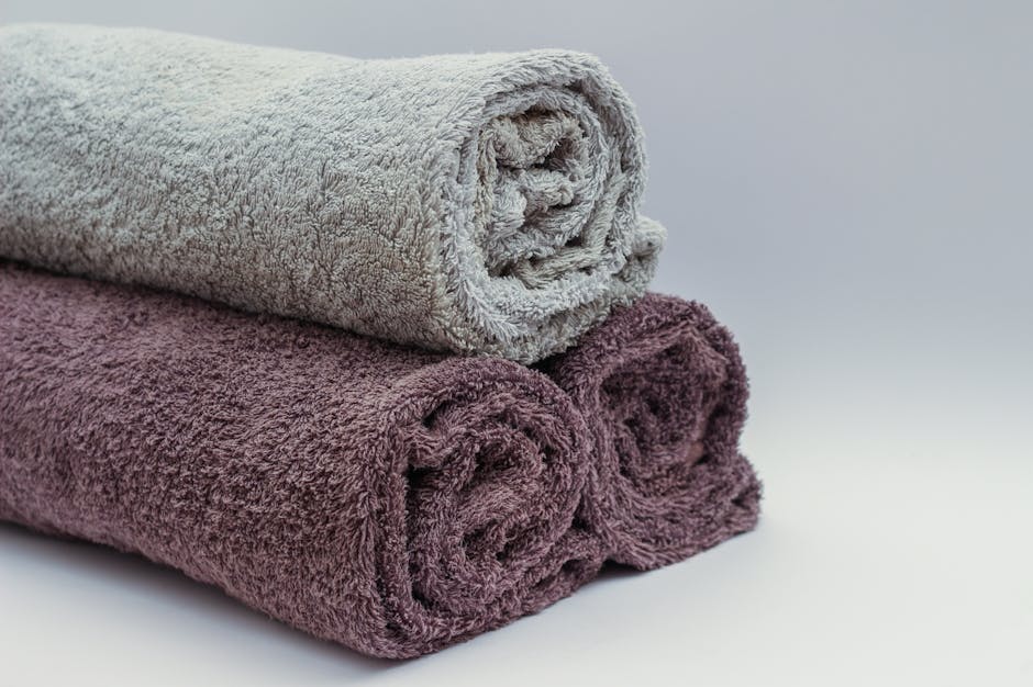 Stack of neatly folded premium designer bath towels in neutral tones on a white shelf
