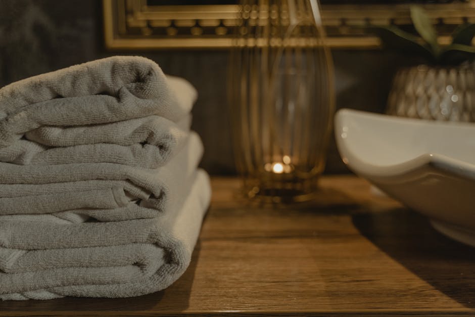 Neatly folded luxury white towels and a plush bath robe on a wooden bathroom shelf