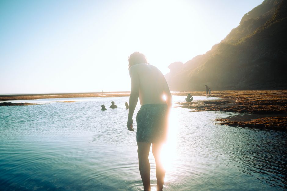 Backlit view of a man standing in shallow waters at sunny beach. Vacation vibes.
