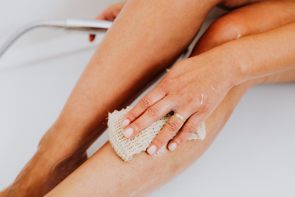 Exfoliating body scrub and loofah on a bathroom shelf, used as prep before self-tanning