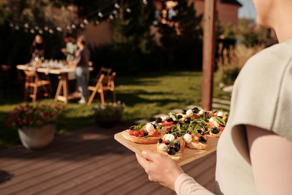 A flat lay of outdoor picnic accessories including tumblers, bamboo plates and a folded blanket arranged on a wooden surface