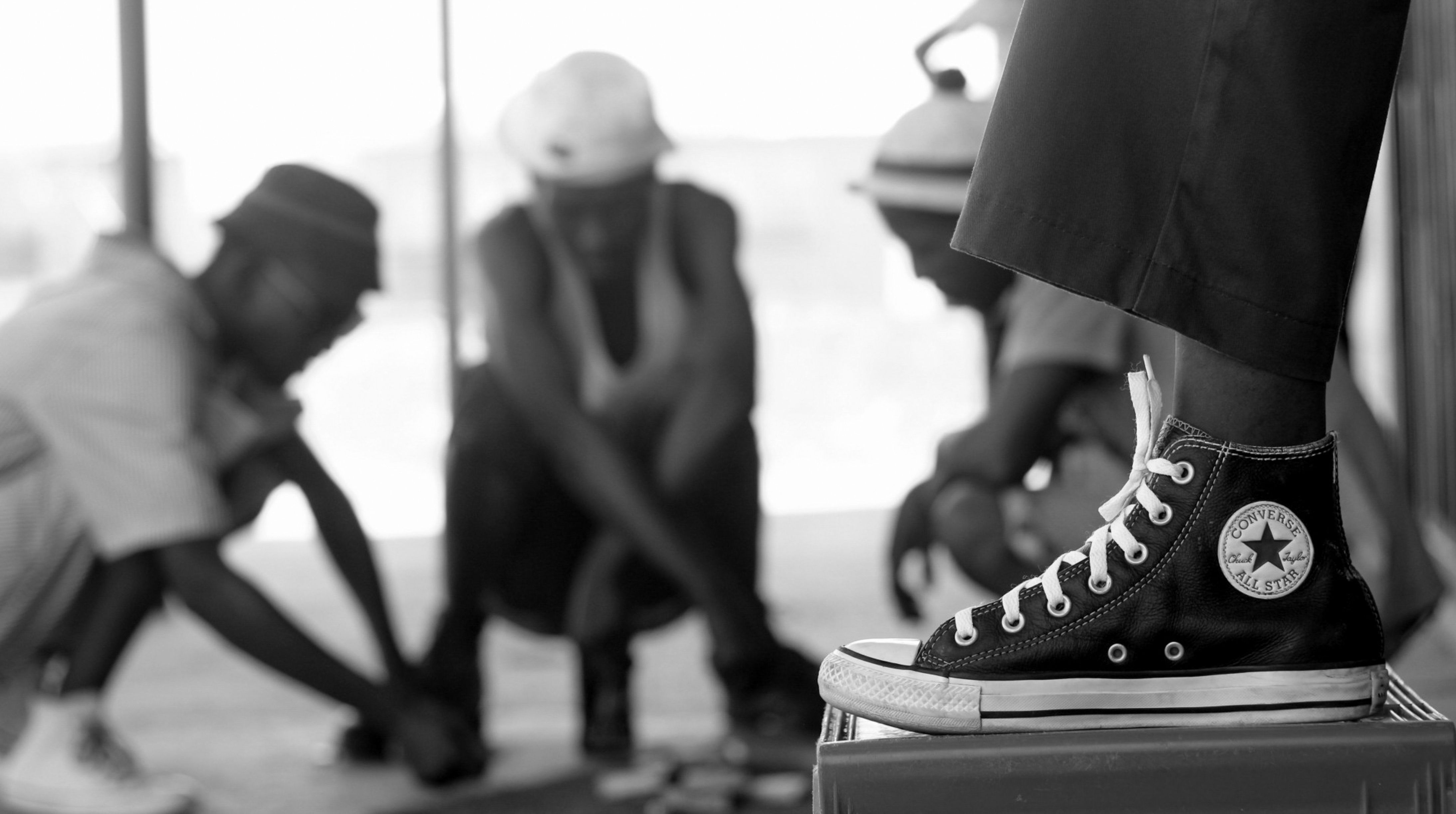 Black and white image of people playing a game with a focus on a Converse shoe.