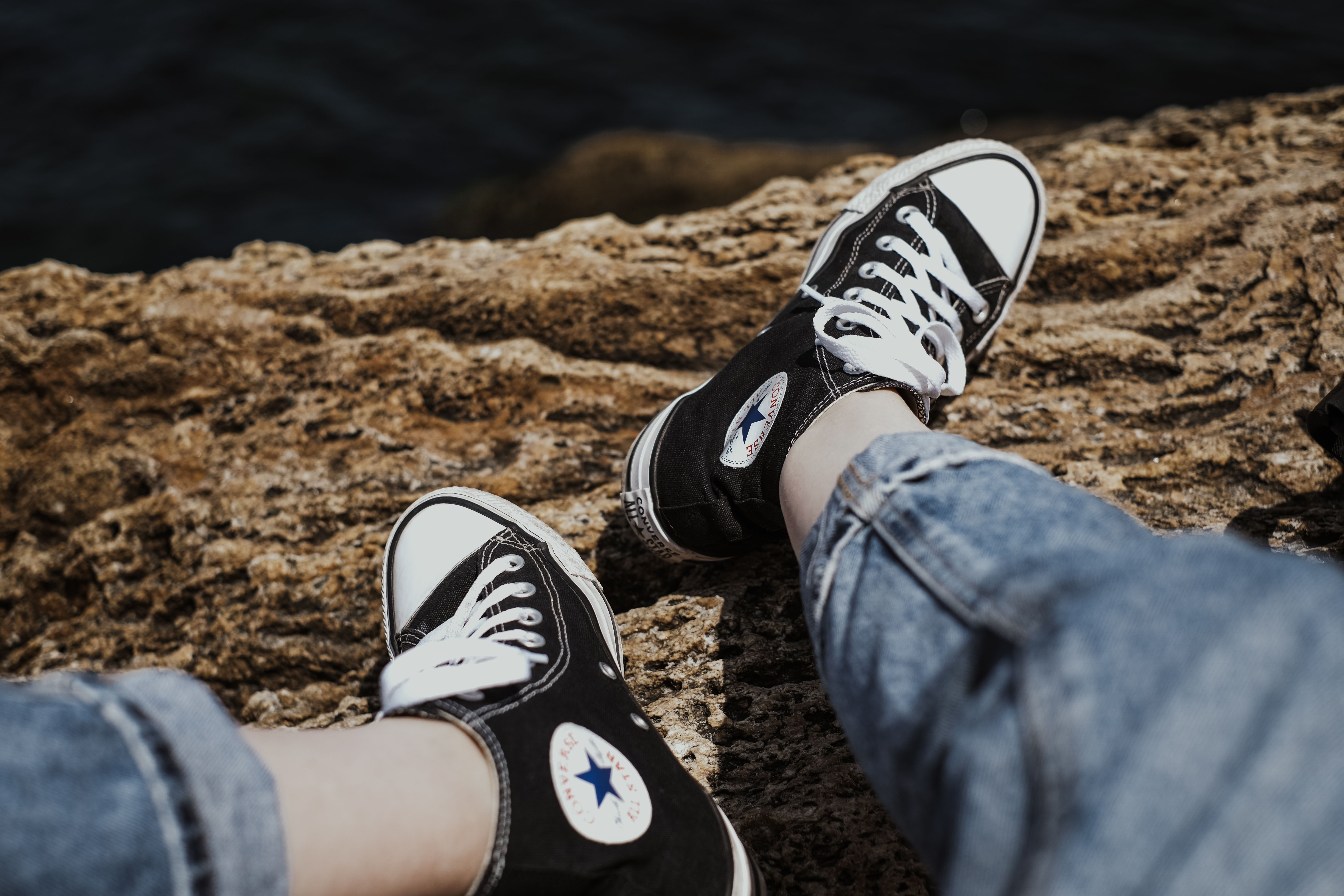 Black Converse sneakers resting on rocks with a casual vibe by the water.