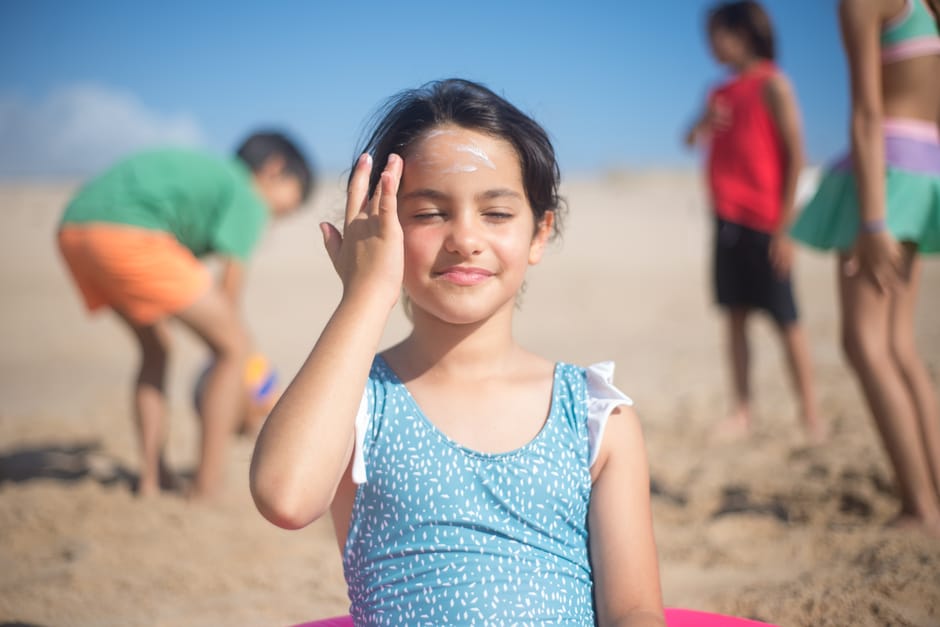 Woman applying SPF moisturiser to her face in bright summer sunlight