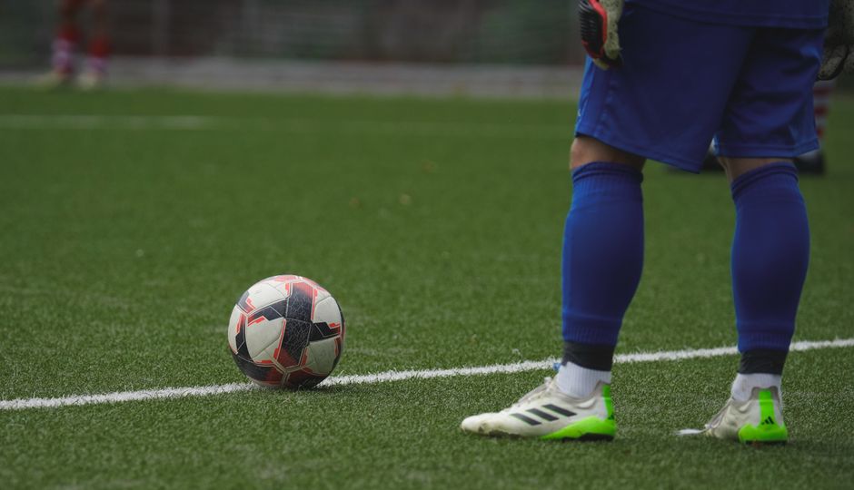 Close-up of a pair of football boots on a natural grass pitch, showing firm ground studs on the outsole