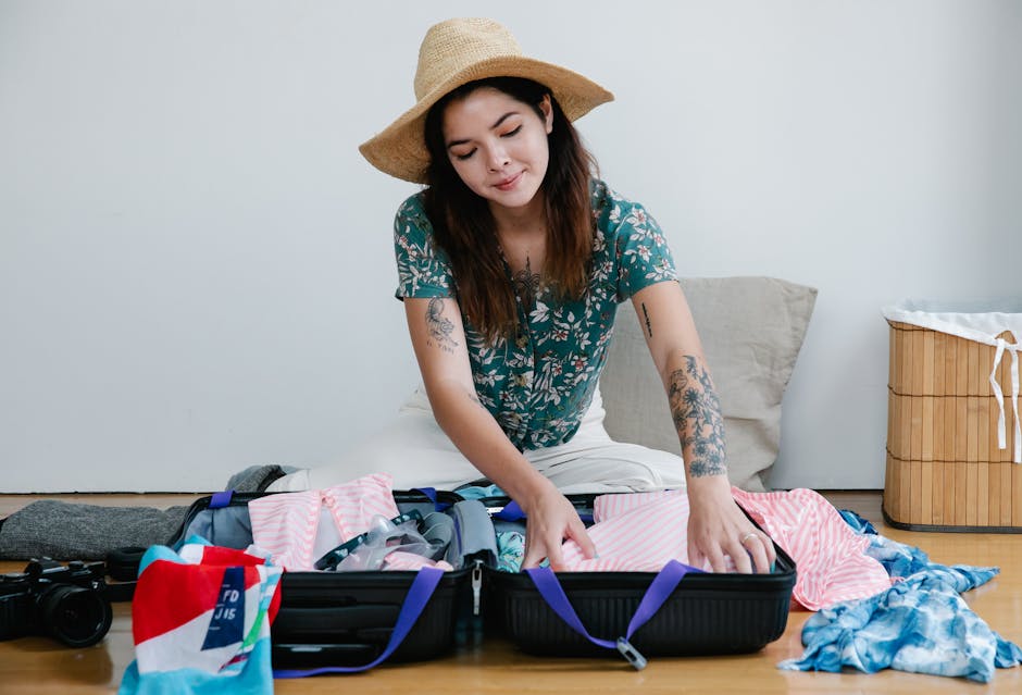 Open suitcase packed with stylish summer holiday clothes in neutral tones on a white bed