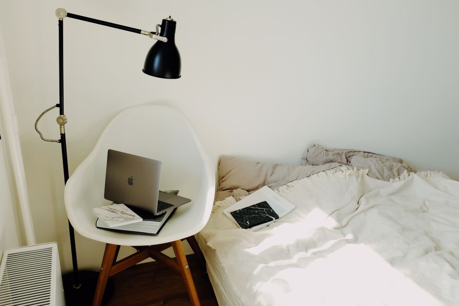 Minimal hotel-style bedroom with neatly folded white sheets, two pillows and a folded throw at the foot of the bed