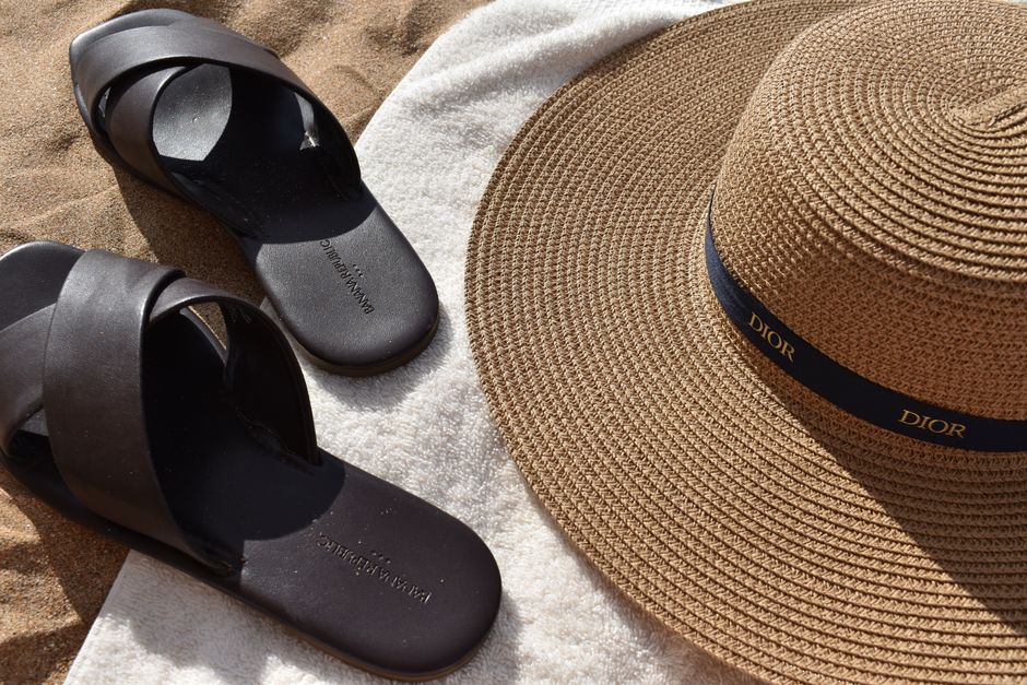 Minimal summer accessories including flat sandals and delicate gold jewellery laid out on a light background