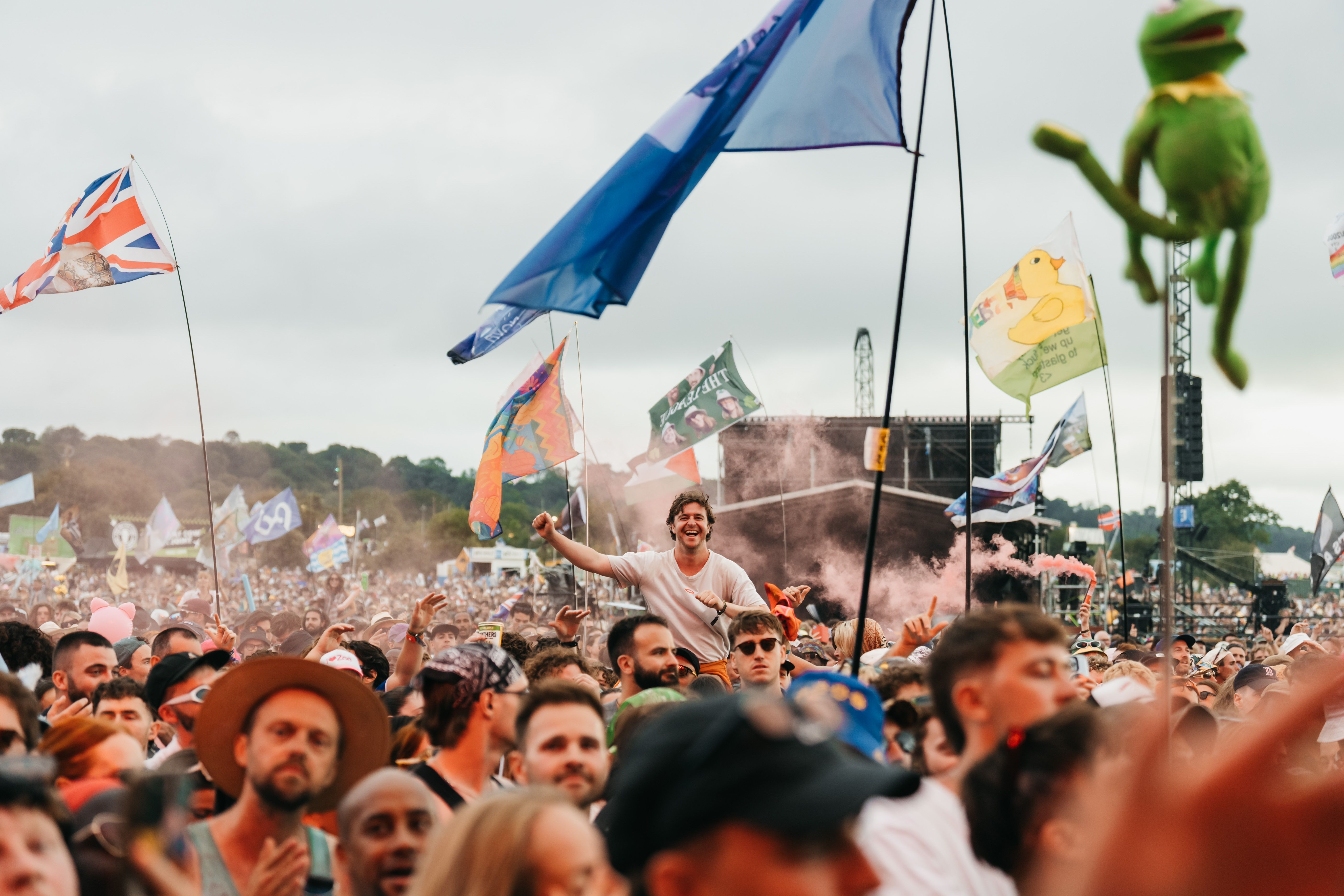 Energetic crowd and colorful flags at Glastonbury Festival in England, showcasing joy and unity.