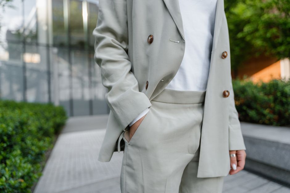 Person in beige blazer and white shirt with hand in pocket outdoors.