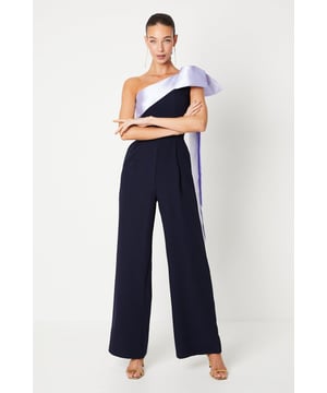 One-shoulder design with a dramatic bow detail
Wide-leg jumpsuit silhouette with a flattering waist tie
crepe fabric with a luxurious drape
Sleeveless bodice with a fitted waist
Full-length wide legs for an elegant, flowing look

Exuding sophistication and glamour, this jumpsuit is a showstopping choice for formal occasions. The one-shoulder neckline with a striking bow detail adds a touch of drama, while the crepe fabric drapes beautifully for a refined look. Style it with statement jewellery and heels for a wedding or evening event, or pair it with a fascinator and clutch for a day at the races. With its flattering waist tie and flowing wide legs, this jumpsuit is sure to turn heads and make a lasting impression.