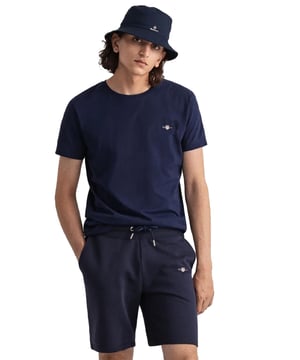Gant introduces a mens t-shirt and shorts set with a small-scale embroidered shield graphic on the chest. Made of soft cotton and featuring a ribbed neckline, this tee showcases the iconic GANT logo. Crafted for everyday wear, the regular-fit tee is both comfortable and sustainable with Better Cotton. The included sweat shorts, also made of soft cotton blend, feature a ribbed waistband, three pockets, and a drawstring waist. The shorts are adorned with a small-scale embroidered shield graphic.