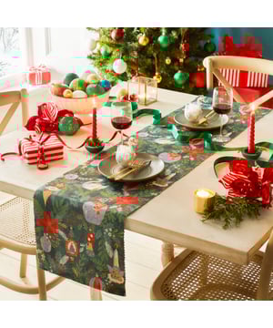 Get into the Christmas spirit with this wonderfully festive table runner. Featuring a digital printed design on woven polyester fabric of Christmas foliage and traditional tree decorations, including vintage baubles, candles and even a swan in vivid seasonal colours. This beautiful table runner will transform and add some instant seasonal cheer to your Christmas dining table.