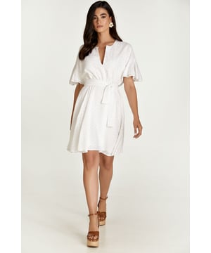 Este vestido blanco está confeccionado en tejido de viscosa bordado tono sobre tono. Tiene mangas cortas con doble volante y hombros caídos. Tiene escote redondo con abertura en V en la parte delantera. Debajo del busto hay una costura curva bajo la cual el vestido se abre en forma de campana. Hay una cremallera oculta en el interior que permite ponerse el vestido fácilmente. Está forrado. El vestido se puede llevar con o sin cinturón que está confeccionado en el mismo tejido. El cinturón está incluido.