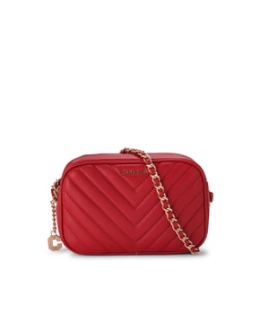 The Carvela Lola Cross Body features a red exterior with chevron stitch detail. The front features gold tone Carvela branding and there is an Icon C charm on one side. Dimensions: 14cm (H), 21cm (W), 7cm (D). Strap drop cross body: 114cm.