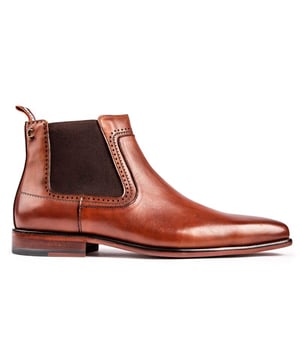 Botas Chelsea sin cordones Simon Carter Terrier color canela para hombre con parte superior de cuero liso. Refuerzos elásticos dobles y detalles de puntadas delicadas. Estos botines premium tienen una puntera alargada. Tirador del talón con la marca y forro de cuero y estampado exclusivo de Simon Carter Queuing Dog. rematado con suela sintética.