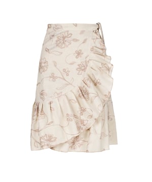 Esta falda cruzada floral de color crudo está confeccionada en un tejido de mezcla de lino y bordada con un hilo bicolor en crudo y beige. La falda se abrocha con una corbata de 4,5 cm del mismo tejido que pasa a través de un agujero en la costura lateral, justo debajo de la cintura. La falda tiene un ribete de volantes de 26 cm por todas partes. Tiene un estilo sutil con una silueta de línea A y llega hasta la rodilla.