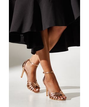 Elegant lattice front design for a sophisticated look
        High heel measuring between 7-9cm for a statuesque silhouette
        Ankle strap with buckle fastening for secure fit
        Wide fit construction for enhanced comfort
        Versatile metallic finish complements various outfits
    
    Step into elegance with the Tilda Lattice Front High Heeled Sandals from Coast. These stunning wide fit sandals are designed to make a statement at any formal occasion. The intricate lattice front detail adds a touch of glamour, while the ankle strap ensures a secure and comfortable fit throughout your event. Perfect for weddings, races, or sophisticated soires, these sandals will effortlessly complement your ensemble. Style them with a flowing maxi dress for a romantic look, or pair with a tailored jumpsuit for a modern twist on occasion wear. The metallic finish allows for versatile styling, making these sandals a go-to choice for various formal events in your social calendar. With Coast's commitment to elegance and quality, these sandals are sure to become a treasured addition to your wardrobe, ready to dazzle at your next special occasion.