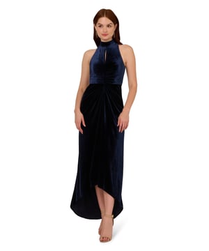 Whether the guest of the hour or just on the guest list, this velvet high low gown will have all eyes on you. This formal dress features a halter bodice with a mock neckline, a cutout at the centre of the bust, and a high low mermaid skirt. Made with luxe velvet, this evening gown is shirred through the body and draped at the hip of the skirt for a figure-flattering look. A hidden zipper closure at the centre back of this sleeveless gown completes the design. Styled with nude heels and statement earrings, this hater gown is ready for a glam evening.