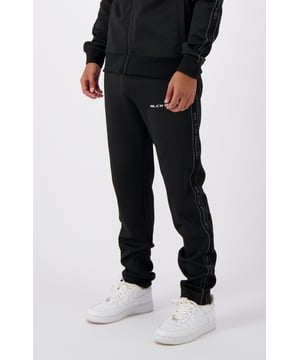 Pantalones de chándal de pierna ancha 100 % poliéster Cintura elástica con cordón Dos bolsillos delanteros Cinta de marca BLACK BNNS en los laterales Logotipo BLACK BNNS en la pierna izquierda Se puede combinar con TAPED INITIAL TRACKTOP