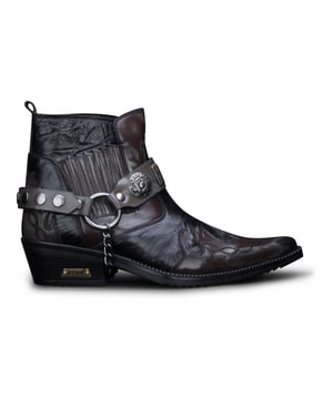 El winklepicker es un estilo popular de botas, usado desde la década de 1950 y un favorito entre los artistas británicos de rock and roll a lo largo del tiempo. Este par se completa con la característica distintiva del winklepicker, que es la punta afilada, así como la silueta tradicional de botín y un tacón cubano vintage de 2". Un diseño texturizado aparece en todo el zapato, con diseños de paneles cosidos en la punta y el talón, así como un diseño con volantes en los lados. Esta bota se completa con la adición de una característica de correa de arnés triple, que está conectada por un anillo de metal y presenta insignias metálicas y tachuelas para crear una estética llamativa. • Elaborado con cuero de vaca genuino • Presenta una distintiva punta puntiaguda, un tacón cubano de 2" y una caña alta hasta el tobillo • Característica de correa metálica de arnés triple • Marca ETOR adornada en la suela