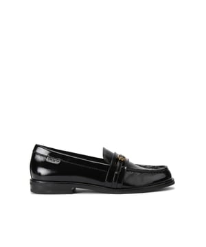 The Kurt Geiger Mayfair Slim Loafer features a black patent upper with a thin strap across the toe. There is an antiqued brass buckle with micro eagle head surrounded by crystals fastening the strap.