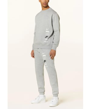 Nike Club Fleece+ trainingspak met meerdere logo's in donkergrijs gemêleerd. Een frisse nieuwe bewerking van de klassieke en geliefde clubcollectie, een esthetiek met meerdere logo's en bedrukte details op het sweatshirt en de joggingbroek. Glad aan de buitenkant en gezellig aan de binnenkant: geborstelde fleece is perfect voor casual kleding en loungewear. Ontspannen tot aan de schouders, borst, lichaam, taille en benen voor een gemakkelijke pasvorm.