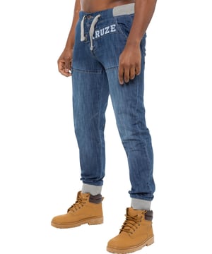 Kruze Designer-Herren-Jogger-Jeans mit Gummizug am Bund. Fliegender Knopfverschluss. Zwei Vordertaschen und zwei Gesäßtaschen. Markenknöpfe und Nieten. Branding auf Vorder- und Rückseite.
