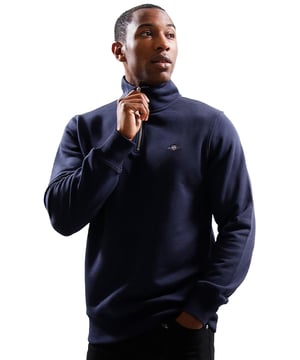 This versatile half-zip sweatshirt combines comfort and style with a premium cotton-polyester blend that's perfect for transitional weather. Featuring a small, intricately embroidered GANT graphic on the chest, it showcases a subtle yet elevated design. The ribbed hem and cuffs create a tailored silhouette. Designed for a regular fit, the half-zip collar adds a touch of sporty elegance, while the durable fabric ensures long-lasting wear.
