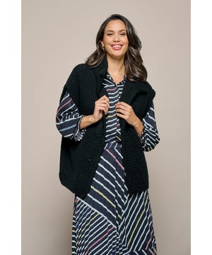 Voor een elegante winterlook kies je dit mouwloze gebreide vest. Het Isra-vest in een klassieke zwarte kleur is een veelzijdige aanvulling op je garderobe. Dit vest biedt extra warmte en een speelse uitstraling door het grof gebreide wol. Het heeft blinde drukknopen, een dikke kraag, een openvallend ontwerp en grove ribboorden. Met een losse pasvorm en een lengte die net op de heup valt, biedt het zowel comfort als stijl. Dankzij de hoogwaardige materialen is dit vest een uitstekende keuze voor je wintergarderobe. Combineer het met een blauwe jeans en een witte blouse voor een casual chique look, of draag het over een elegante tuniek voor een modieuze uitstraling. Ervaar de tijdloze charme en het comfort van de gebreide vesten van Mart Visser!