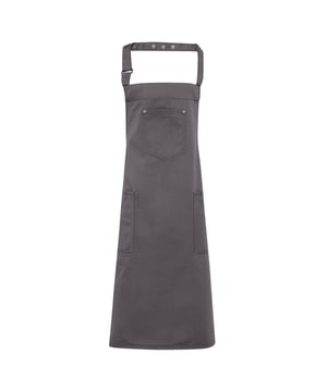 Eine Schürze im Chino-Stil mit vollem Latz. Eine aufgesetzte Tasche mit Nieten befindet sich oben in der Mitte und zwei Seitentaschen, die groß genug sind, um Tablet-Geräte zu transportieren, sitzen knapp unter der Taille. Der Nackenriemen ist lose und der Träger kann das Ende durch die Schnalle ziehen und die Druckknöpfe zur Befestigung verwenden. Eine coole und ausgefallene Uniformlösung für Bars und Restaurants. Material: 100% Baumwollköper.
