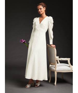 Taking on Thirties-inspired styling, the new Rose wedding dress in our LKB Bridal collection plays to signature LKB design codes. Crafted from luxurious ivory silk with a pretty floral and spot jacquard, it's a maxi style with a V-neck, statement puff shoulders and long sleeves finished with covered buttons. It has a floaty shape, a feminine bow at the back and matching covered buttons. Wear it with a strappy wedding sandal to continue the vintage feel.