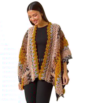 Boucle Pattern Cape from Roman. This style is ONE size.  Stay cosy and stylish this Autumn/Winter season with this boucle pattern cape. Crafted in brown and natural hues, this versatile piece adds a touch of elegance to any outfit. The boucle textured pattern adds a unique touch while the throw-on style makes it effortless to layer over a simple t-shirt and jeans for a chic and polished look.