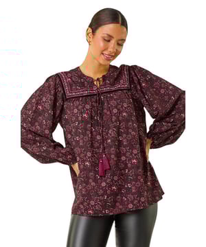 Floral Print Tie Front Top from Roman. Effortlessly chic, this tie front top is a must-have for the Autumn/Winter season. Adorned in an all-over floral print, this top features elegant embroidery details and a tie neck with cute tassel finishes. Long sleeves with elasticated cuffs give a comfortable yet stylish fit. Pair with tailored trousers and heeled boots for a sophisticated look that will take you from day to night seamlessly!
