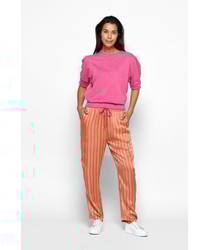 De nieuwste toevoeging aan de Caroline Tensen Collectie betovert met een kleurrijke broek, voorzien van semi-wijde pijpen en gedrukt met levendige oranje en roze strepen, waardoor het perfect is voor de zomer. Met een roze trekkoord bij de taille om de pasvorm aan te passen, twee handige zakken en elegante, vloeiende pijpen biedt deze gestreepte broek een combinatie van stijl en gemak. De Florida broek combineert een gestreepte print met een subtiele glans van modal kwaliteit, waardoor het een relaxte, maar toch verfijnde uitstraling heeft. Voor een volledige look combineer je het met de bijpassende California blouse. Gemaakt van 100% modal, biedt deze broek het hoogste comfort en een weelderige uitstraling.