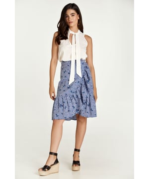 Esta falda cruzada floral está confeccionada en tejido de viscosa estilo denim. La falda se abrocha con una corbata de 4,5 cm del mismo tejido que pasa a través de un agujero en la costura lateral, justo debajo de la cintura. La falda tiene un ribete de volantes de 26 cm por todas partes. Tiene un estilo sutil con una silueta de línea A y llega hasta la rodilla.