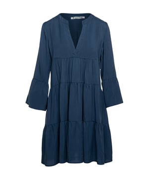 Indigo jurk met geplooide naden van geweven tencel stof. Driekwart klokmouwen. Ronde hals met een V-opening van 24 cm aan de voorzijde. Drukknoop aan de binnenkant onderaan de V om te voorkomen dat deze te veel opent. Langwerpige dubbele stof onder de V-opening aan de voorkant. De jurk heeft twee 24 cm brede, geplooide panelen. Dubbele plooi aan de achterkant. Losvallend A-lijnmodel. Valt boven de knie.