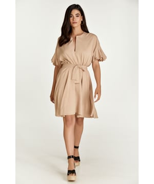 Deze beige jurk is gemaakt van geweven linnen stof. Het heeft korte mouwen met dubbele ruches en hangende schouders. Het heeft een ronde halslijn met een V-opening vooraan. Onder de buste is een gebogen naad waaronder de jurk uitloopt in een clochestijl. Aan de binnenkant zit een verborgen ritssluiting waardoor de jurk gemakkelijk kan worden aangetrokken. De jurk is gevoerd. De jurk kan worden gedragen met of zonder de ceintuur, die in dezelfde stof is vervaardigd. De ceintuur is inbegrepen.