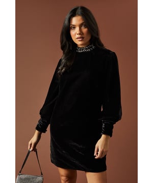 Luxurious velvet fabric for a sumptuous feel
        High neck adorned with sparkling diamante trim
        Elegant swing silhouette for a flattering fit
        Long sleeves with gathered cuffs for added sophistication
        Versatile mini length suitable for various occasions
    
    This enchanting Oasis velvet swing dress radiates elegance and charm, perfect for those special occasions that demand a touch of glamour. The high neck, embellished with a dazzling diamante trim, adds a captivating focal point to the ensemble. The dress's swing silhouette gracefully skims the body, offering both comfort and style. Pair it with strappy heels and a clutch bag for formal events such as weddings or cocktail parties. For a more relaxed yet chic look, style it with ankle boots and statement earrings for an evening out. The versatility of this dress allows for endless styling possibilities, making it a wardrobe staple for the fashion-forward woman who appreciates feminine and pretty designs. Whether you're attending a graduation ceremony or a sophisticated dinner, this Oasis creation will ensure you stand out with effortless grace.