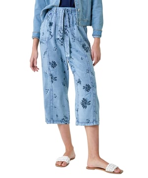 Floral Print Culotte Trousers from Roman. Add a touch of floral flair to your Spring wardrobe with these stylish culotte trousers. Featuring a cute floral print on a denim wash backdrop, these trousers are perfect for the new season. The elasticated waist with a tie belt detail offers both comfort and style, while the cropped culotte length and wide leg shape create a flattering silhouette. The light woven material and pull-on design make them a real Spring staple. Complete your look with a denim jacket, cami top and sandals for effortless daywear.