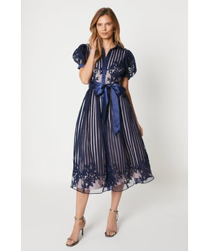 This stunning midi dress features delicate sheer lace detailing, with the contrast blush lining adding a subtle touch of femininity. The organza puff sleeves and satin belt cinch in at the waist, creating a flattering silhouette, while the midi length and shirt dress style make it versatile for both formal and casual events. You'll feel confident and beautiful in this dress.