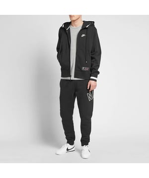 Nike Air trainingspak voor heren met doorlopende ritssluiting in zwart. Capuchon met trekkoord, ritssluiting, geborduurde Swoosh. Gedrukte branding, opgesplitste kangoeroezak. Geweven merkpatch, geribbelde manchetten en zoom. Elastische tailleband. Elastische taille joggingbroek met trekkoord. Geribbelde onderbeenmanchetten voor een comfortabele pasvorm.