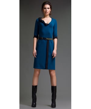 Este vestido está confeccionado en tejido de fieltro bicolor. Tiene mangas al codo y escote en pico con detalle de volante. Los puños y la falda presentan detalles de pasamanería. El vestido tiene una sutil silueta en A.