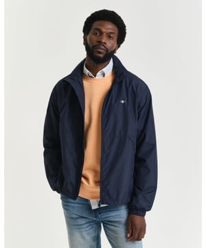 Crafted from 100% recycled polyester and treated with a water-repellent finish, this lightweight windbreaker jacket is perfect for transitional weather. Designed for a regular fit that sits just above the hips, the jacket is fully lined for added comfort. It features a front zip closure, side zip pockets, and a convenient emergency hood tucked into the collar. The design is finished with a reflective GANT logo print at the chest, adding both style and visibility. 

Regular fit
Above hip length
Water-repellent (DWR treatment)
Adjustable drawstring at hem

 Shell - 100% Recycled Polyester, Lining - 100% Recycled Polyester 

7006501
 
 