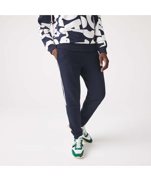 Men's Lacoste Branded Bands Skinny Fleece Joggers.- Brushed cotton blend fleece.- Elasticised waistband.- Tapered fit.- Tapered cut.- Side pockets, ribbed finishes on leg bottoms and Lacoste branding on stripes on sides.- Embroidered green crocodile on hip. Material: 83% Cotton, 17% Polyester. Ref: XH1208166.