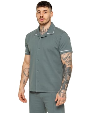 La camisa Enzo para hombre con ribetes es una prenda elegante y versátil, diseñada para ofrecer comodidad y sofisticación. Con un cuello abierto tipo revere y detalles de ribetes blancos a lo largo del cuello y las mangas, esta camisa abotonada ofrece un aspecto refinado pero relajado. Confeccionada con tela premium con elasticidad, garantiza libertad de movimiento sin perder su silueta estilizada. Con un ajuste regular, mangas cortas y un dobladillo cosido, esta camisa es perfecta para salidas informales o un estilo casual elegante.