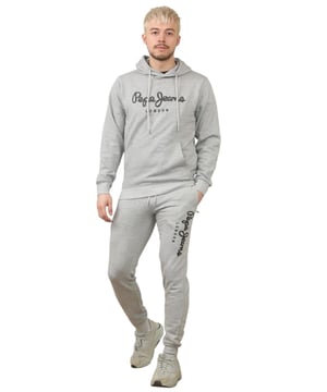 The Pepe Jeans London men's regular fit tracksuit set offers a soft and lightweight hoodie paired with matching joggers. The hoodie features ribbed details on the hood, cuffs, and hem, along with an adjustable hood and a kangaroo pocket for convenience. The joggers come with a waistband drawstring for a secure fit. Both pieces showcase the Pepe Jeans London Big logo on the chest for the hoodie and the left leg for the joggers. A decorative inner neckband with an all-over logo adds a stylish touch. Made from 100% sustainable cotton, the fabric consists of 65% cotton and 35% polyester. The set is a washable machine for easy maintenance.
