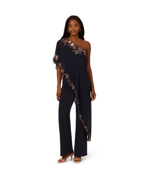 Dynamic, dramatic, and utterly modern, this navy-blue women’s jumpsuit updates our classic beaded look with a one shoulder neckline and asymmetrical cape overlay that falls from the shoulder strap to the hem of the wide leg trousers. Contrasting beaded details trim the edges of the cape in a botanical design for a sparkling finish. An effortless outfit-in-one, you will be instantly ready for your next big event just zip up in the back and go.