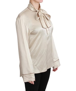 Merk: Dolce & Gabbana  
Staat: Nieuw met labels  
Authenticiteit: 100% Authentiek  
Stijl: Blouse met lange mouwen  
Materiaal: 100% Zijden satijn  
Kleur: Beige  
Borduursel: QUEEN op de linkerborst  
Sluiting: Kraagknop  
Hals: Sjaalkraag met strik  
Details: Logo-details  
Oorsprong: Gemaakt in Italië