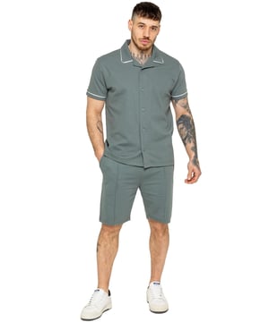 Het Enzo heren trainingspak met piping shirt en shorts biedt een stijlvolle en comfortabele look. Het overhemd met knopen heeft een reverskraag en witte biezen langs de kraag en mouwen voor een verfijnde uitstraling. Gemaakt van stretchstof, zorgt het voor flexibiliteit en een slanke pasvorm. Gecombineerd met bijpassende stretchshorts, biedt deze set comfort en functionaliteit met een elastische tailleband, verstelbaar trekkoord en meerdere zakken. Perfect voor casual uitjes of ontspannen in stijl.